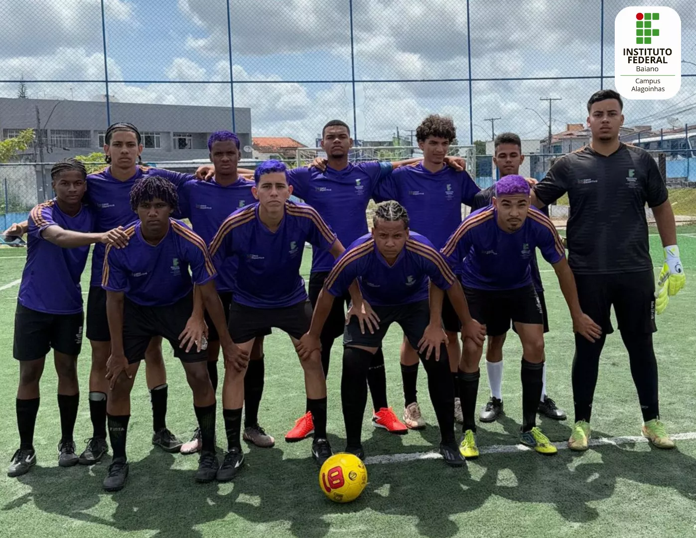 Discentes estão num campo gramado posando em fila com roupas do time na cor roxa e com uma bola de futebol à frente.